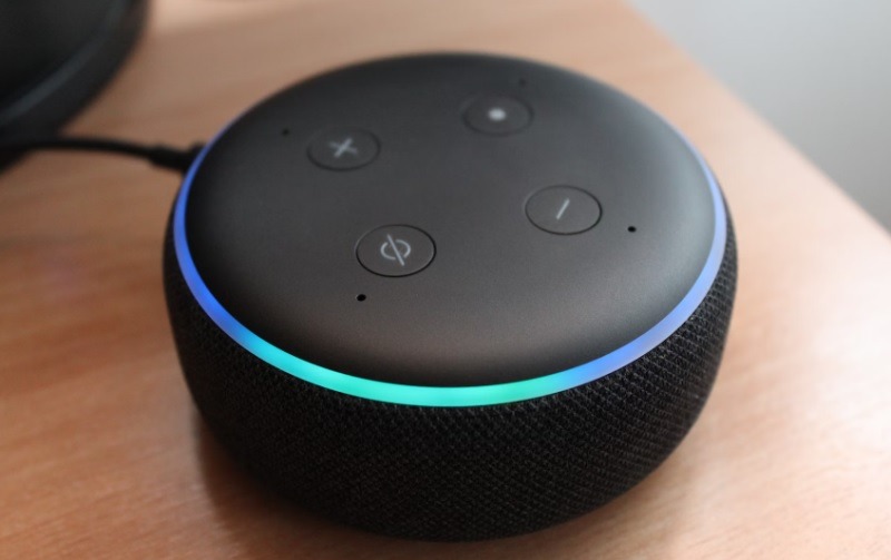 An Amazon Echo Dot sitting on a wood table.