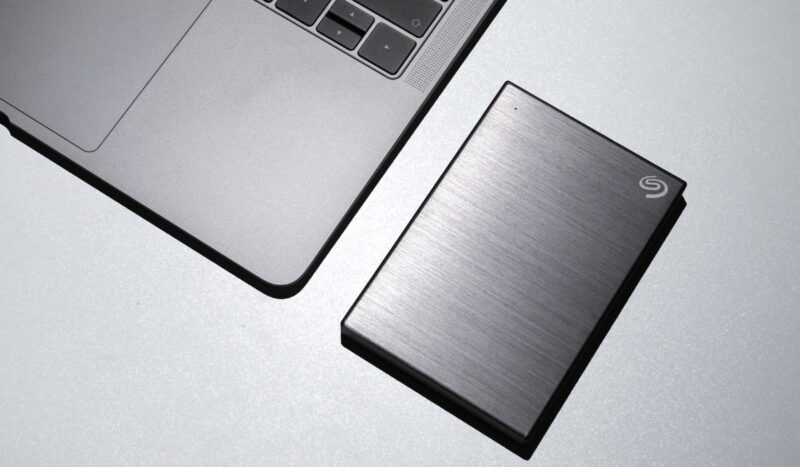 Black external hard drive on a white surface next to a laptop