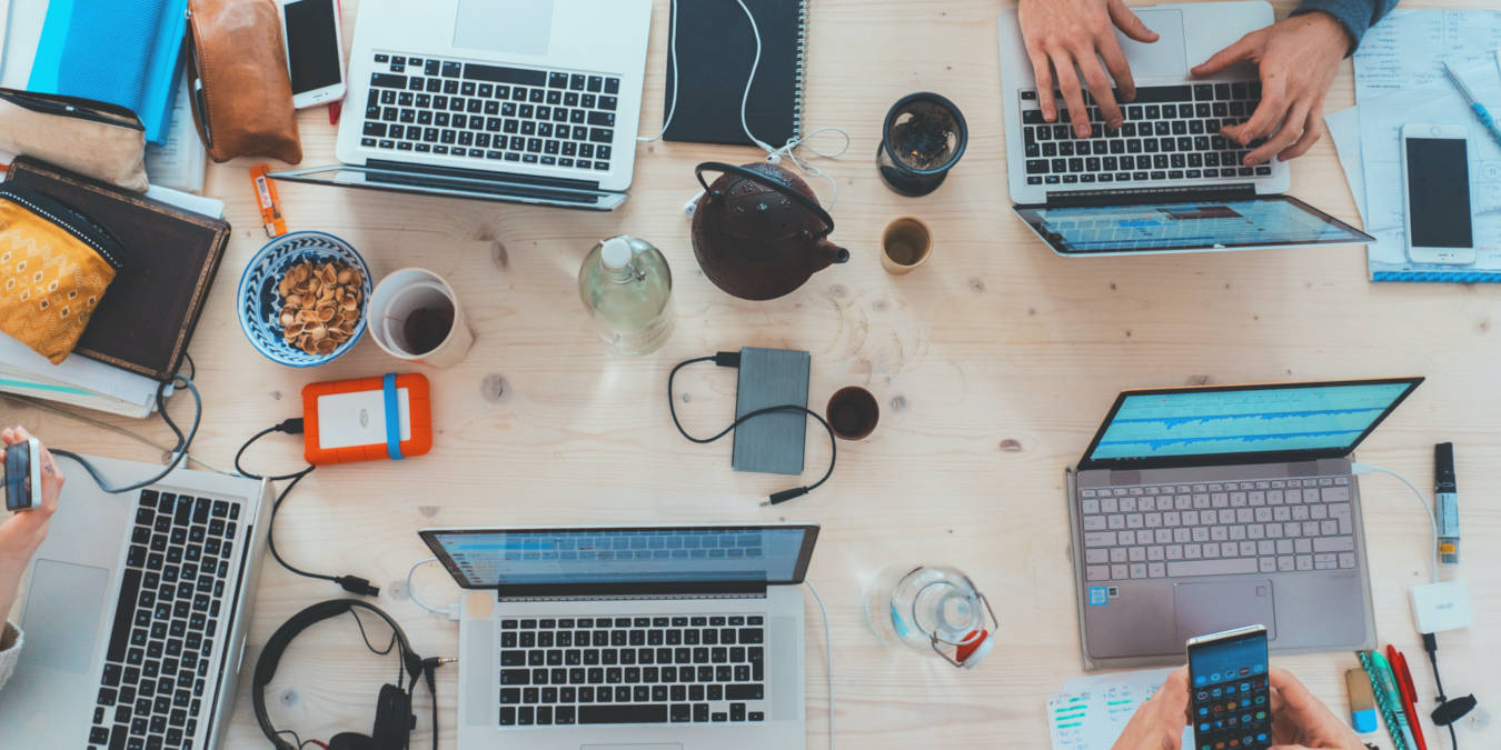 A photograph of a table filled with laptops and people working on laptops.