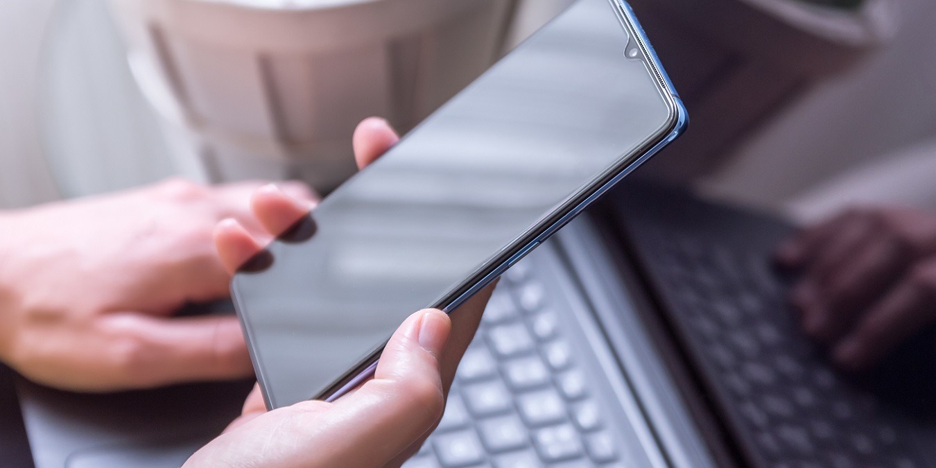 Vertical Shot Of A Female Hand Holding A Smartphone And Laptop